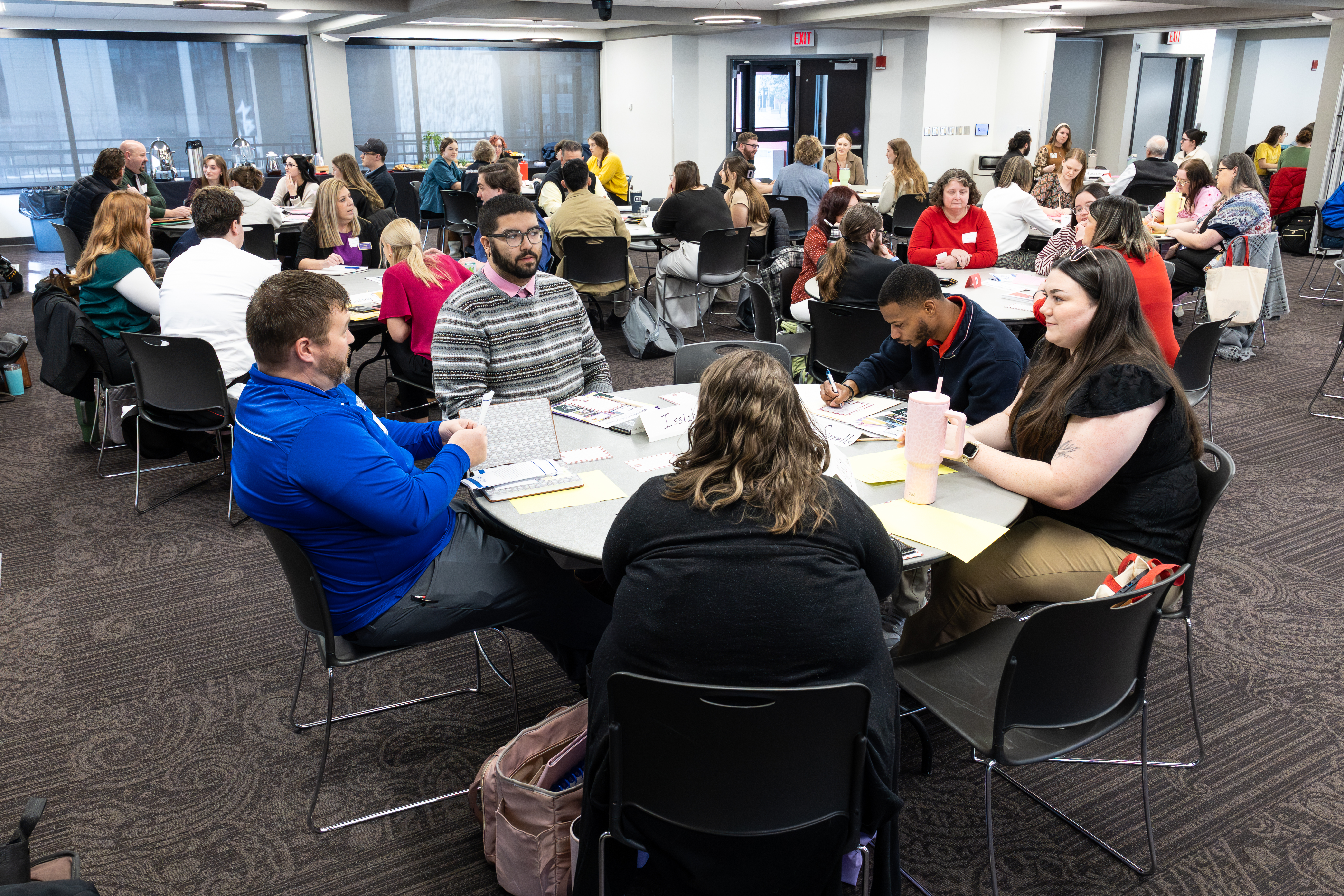 A room full of educators sit around tables to collaborate
