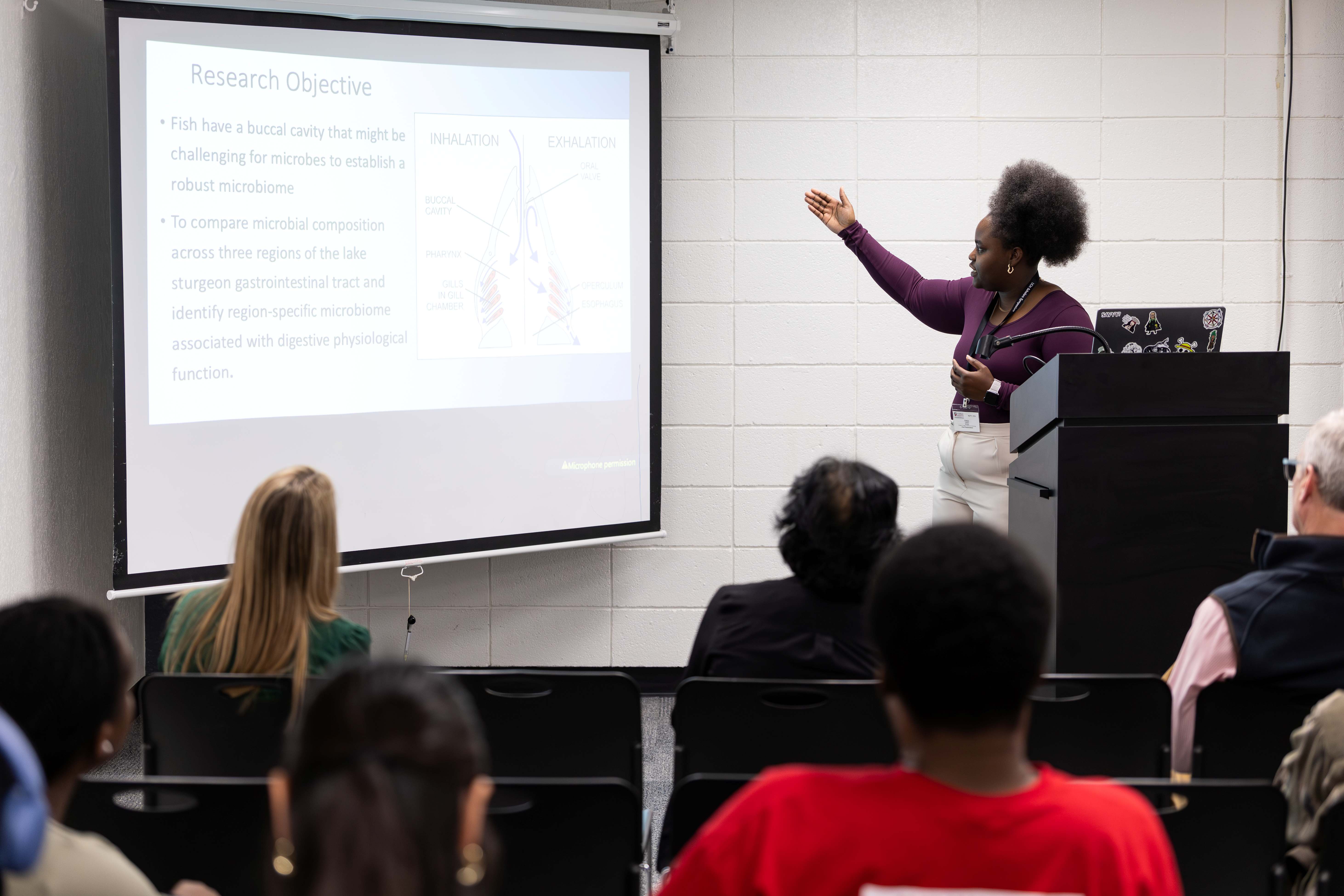 Student pointing at her slideshow in front of an audience.