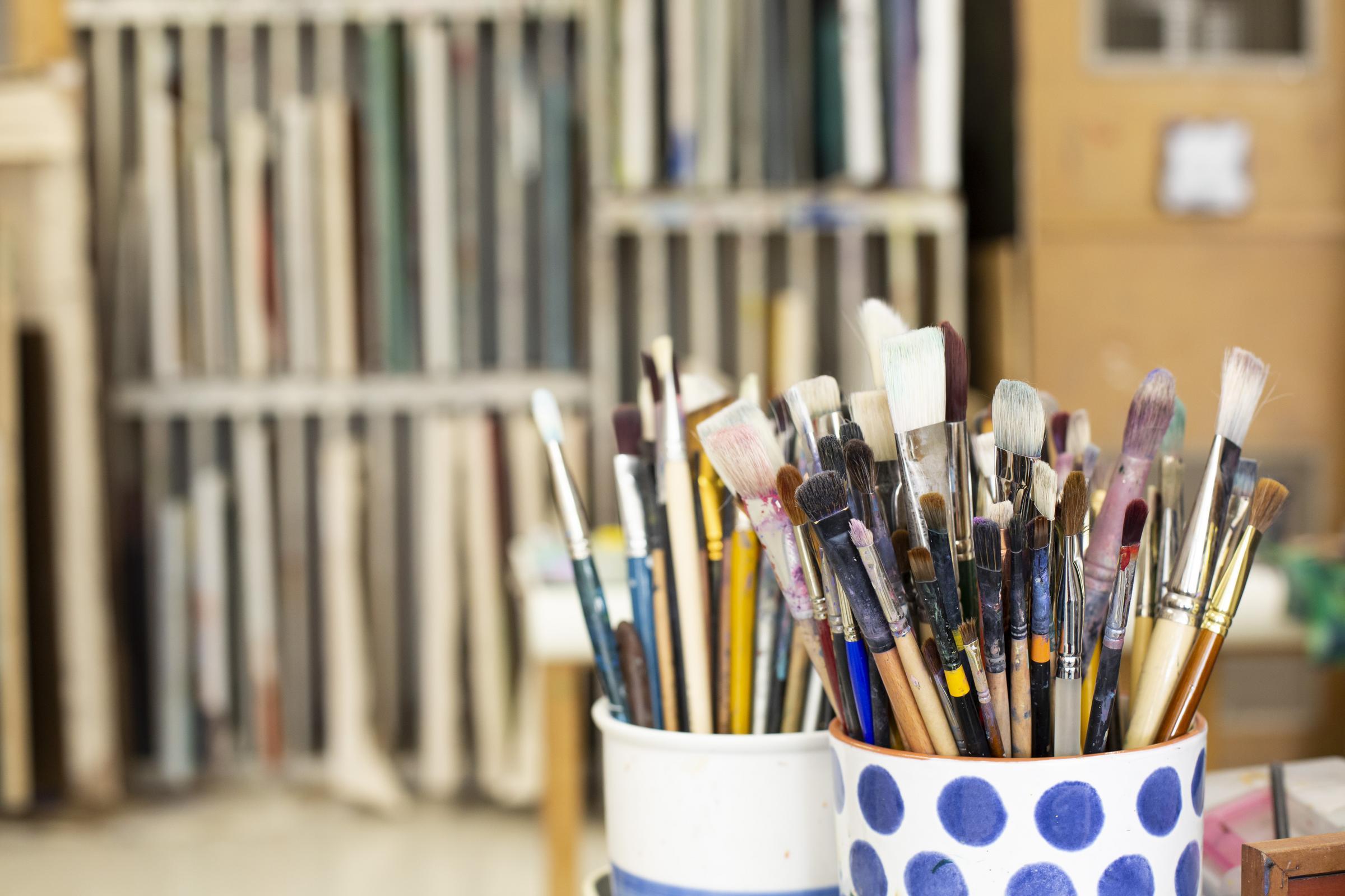 Numerous paintbrushes are gathered in a cup in the art studio