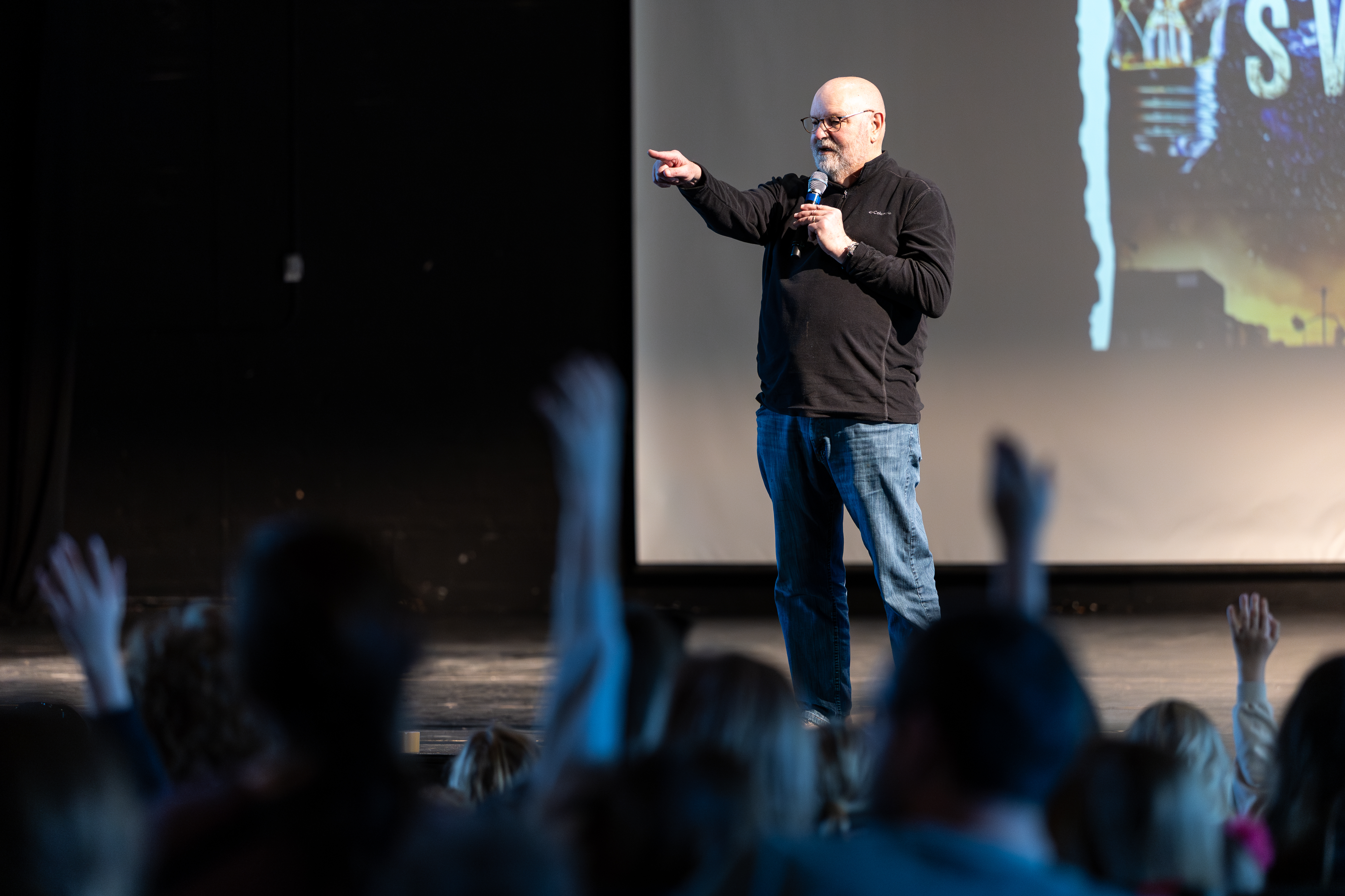 Author standing on stage points into a crowd of students with their hands raised