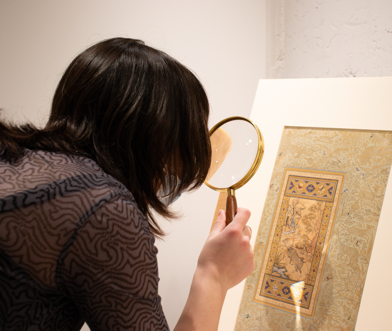 Image of an Honors College student looking through magnifying glass at a piece of art.