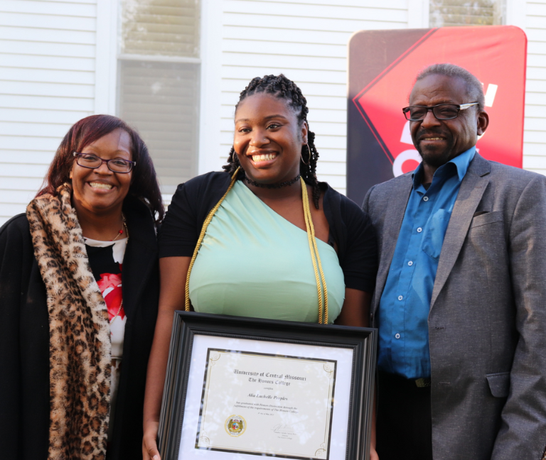 Image of an Honors College student receiving an honors certificate standing inbetween her parents.