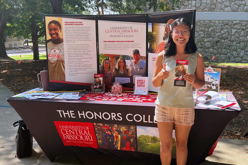 Honors student in front of promotional table.